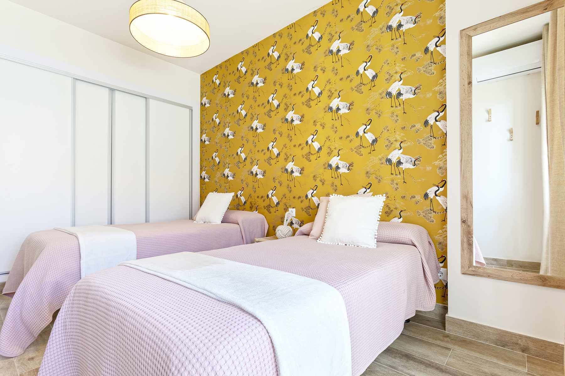 Una habitación de hotel con dos camas, una pared amarilla con diseño y un espejo grande.
