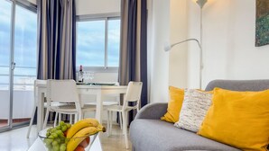 A dining area with a table set for two, a bowl of fruit, and a grey sofa with yellow cushions. - Club Maritimo Front line Beach Apartments (Fuengirola)
