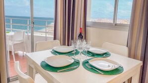 A dining table set with plates, cutlery, and a bottle of wine, overlooking a beach and ocean view. - Club Maritimo Front line Beach Apartments (Fuengirola)