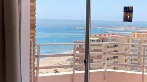 Uma varanda com vista para a praia e o oceano, duas cadeiras estampadas e uma mesa.