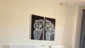 A hotel room with two beds, a nightstand with a lamp, and two wall-mounted paintings.