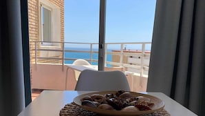 A table with a woven placemat and a plate of seashells, overlooking a balcony with a clear view of the sea. - 95 - Club Maritimo Sea View (Fuengirola)