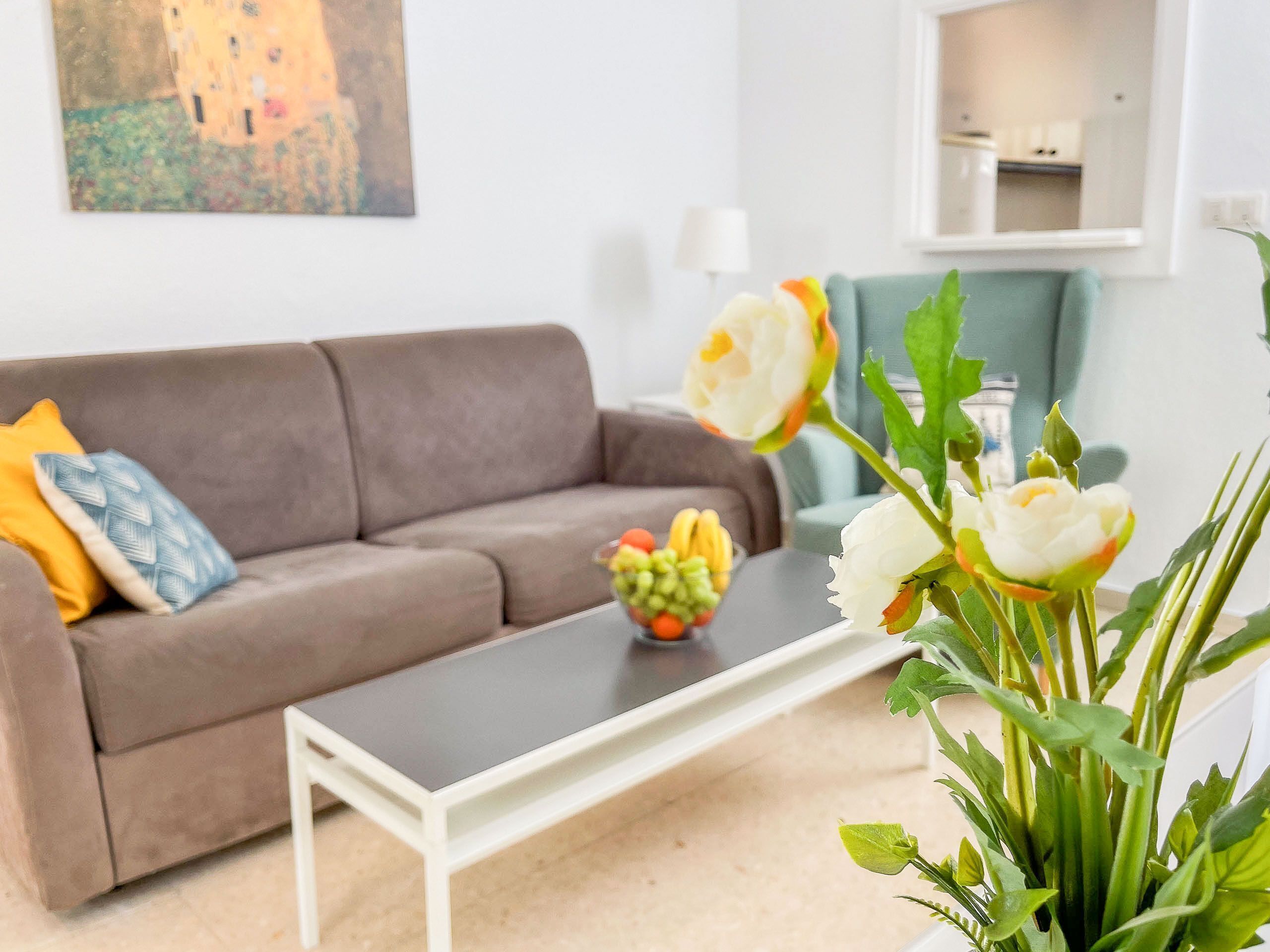 Una sala de estar con un sofá marrón, una mesa de centro blanca y un jarrón con flores.