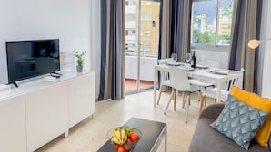 A modern apartment with a flat-screen TV, dining area, and a balcony with a view of the city.