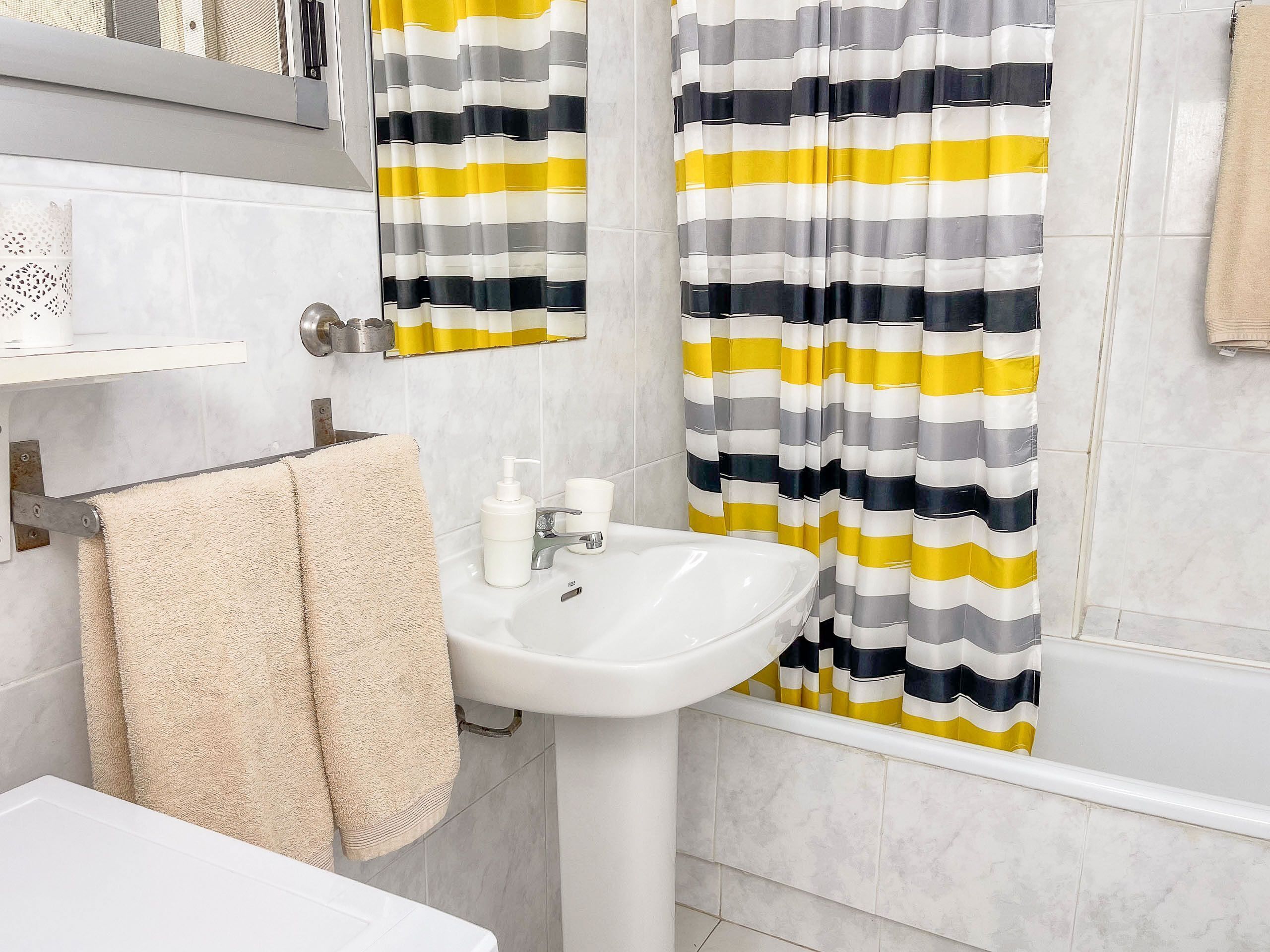 Une salle de bain avec un lavabo blanc, un miroir et des rideaux de douche à rayures.