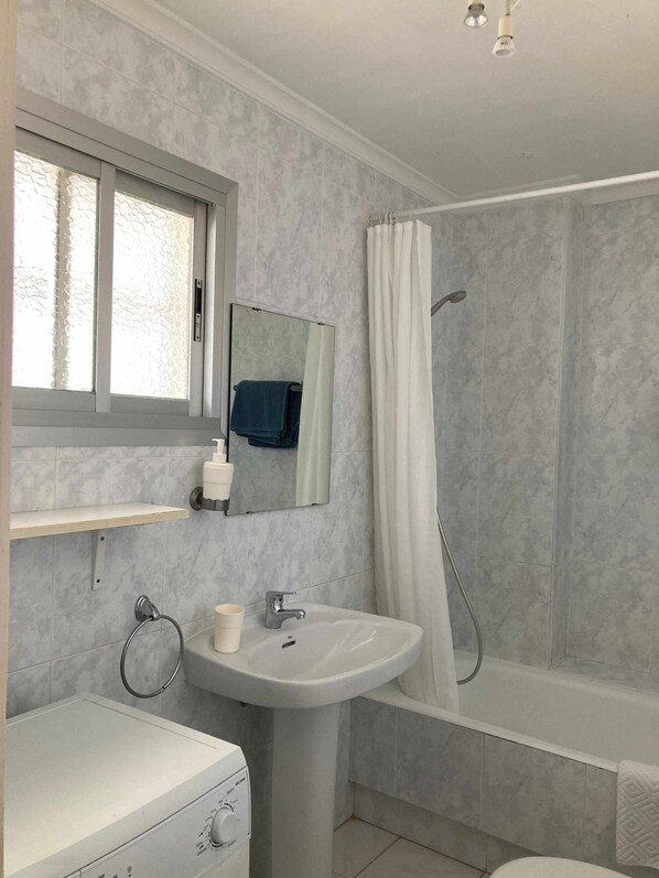 Une salle de bain avec un lavabo blanc, un miroir, un porte-serviettes, une fenêtre et un espace douche.