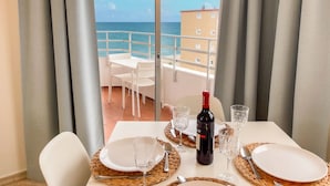 A balcony with a table set for two, a bottle of wine, and a view of the sea and buildings.