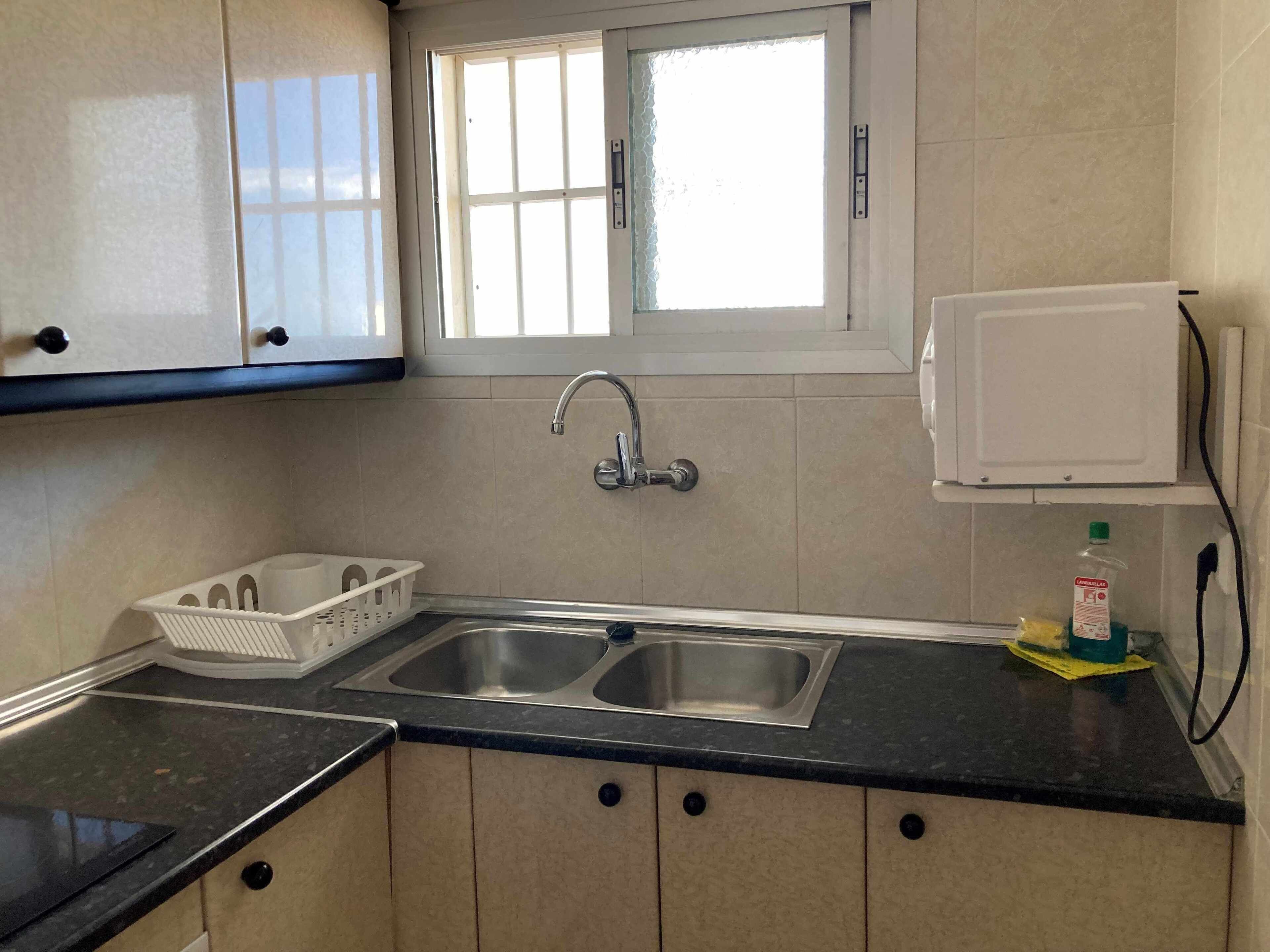 A kitchen with two sinks, a window, cabinets, and a microwave.