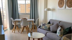 Un salon moderne avec un canapé gris, une table basse ronde et un coin repas comprenant une table et des chaises blanches.