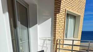 A balcony with two chairs and a table, overlooking a beach.