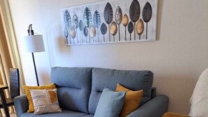 A living room with a grey sofa, a wooden coffee table, a yellow armchair, and a wall art piece above the sofa.