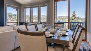 Comedor con una mesa preparada para cuatro, ventanas amplias con vistas a la montaña y una zona de estar acogedora con un sofá.
