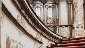 Una imponente escalera con barandales y columnas decorativas, que conduce a un arco de entrada.