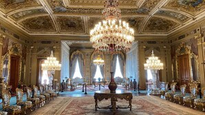 Una habitación opulenta con candelabros ornamentados, espejos con marcos dorados y una larga fila de sillas de diseño intrincado.