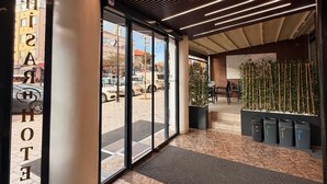 Un vestíbulo de hotel con diseño moderno, que cuenta con una amplia entrada de vidrio, un techo de madera con iluminación lineal y vistas a la calle.