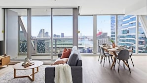 Un soggiorno moderno con vista sulla città, un'area pranzo con tavolo e sedie e un divano con cuscini.