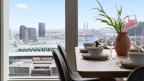 Tavolo da pranzo apparecchiato con piatti, ciotole e un vaso con una pianta, con vista su un paesaggio urbano che include un ponte e degli edifici.