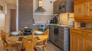 A modern kitchen with wooden cabinets, stainless steel appliances, and a dining area with wooden chairs and a table set for two. - Cozy 3-Room Ski-In Apartment for 6 in La Daille, Val d'Isère with Balcony and Parking (Val-d'Isère)