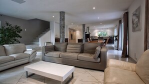A modern living room with a neutral color palette, featuring a sectional sofa, a coffee table, and a staircase leading to an upper level.