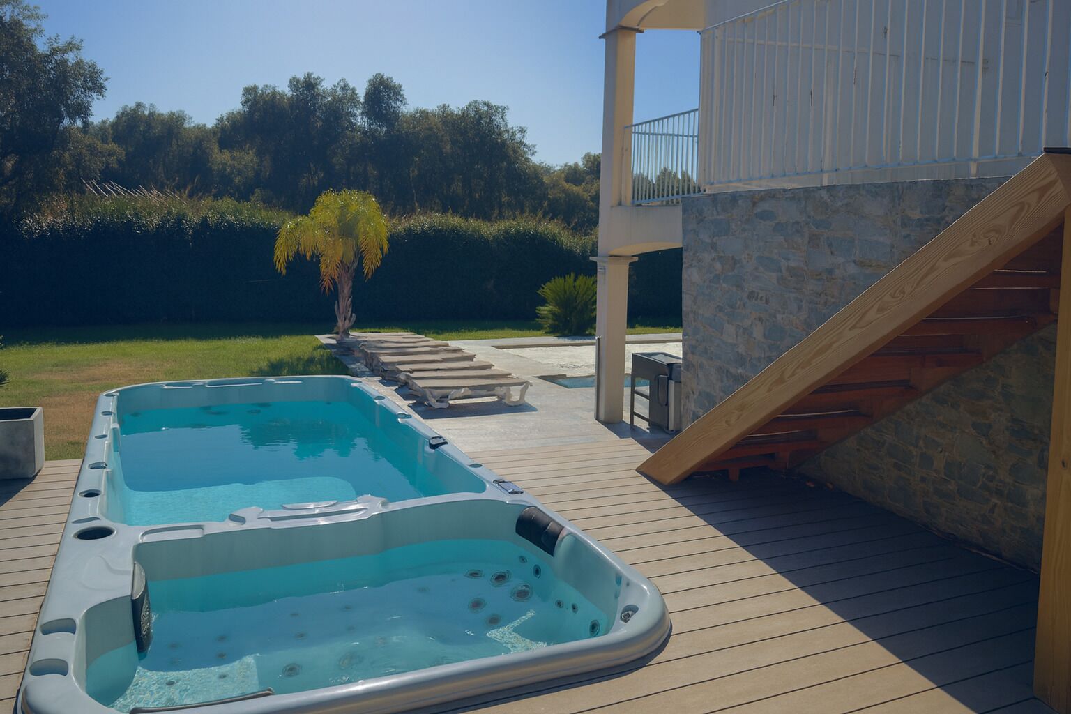 A swimming pool area with two hot tubs, a wooden deck, and a stone wall.