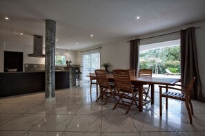 A modern kitchen with a central island, a dining area with wooden chairs, and a large window with curtains.