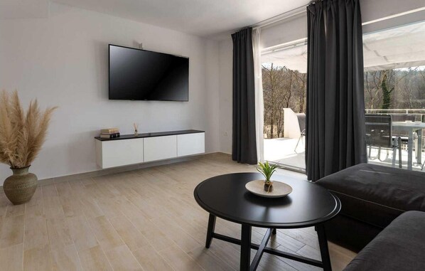 A modern living room with a flat-screen TV mounted on the wall, a round black table with a plant, a sofa, and a white cabinet below the TV. - 2 bedroom beautiful home in Pazin (Pazin)