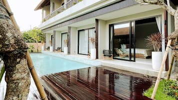 Una casa moderna de dos pisos con una terraza de madera, una piscina y un balcón con plantas en macetas.