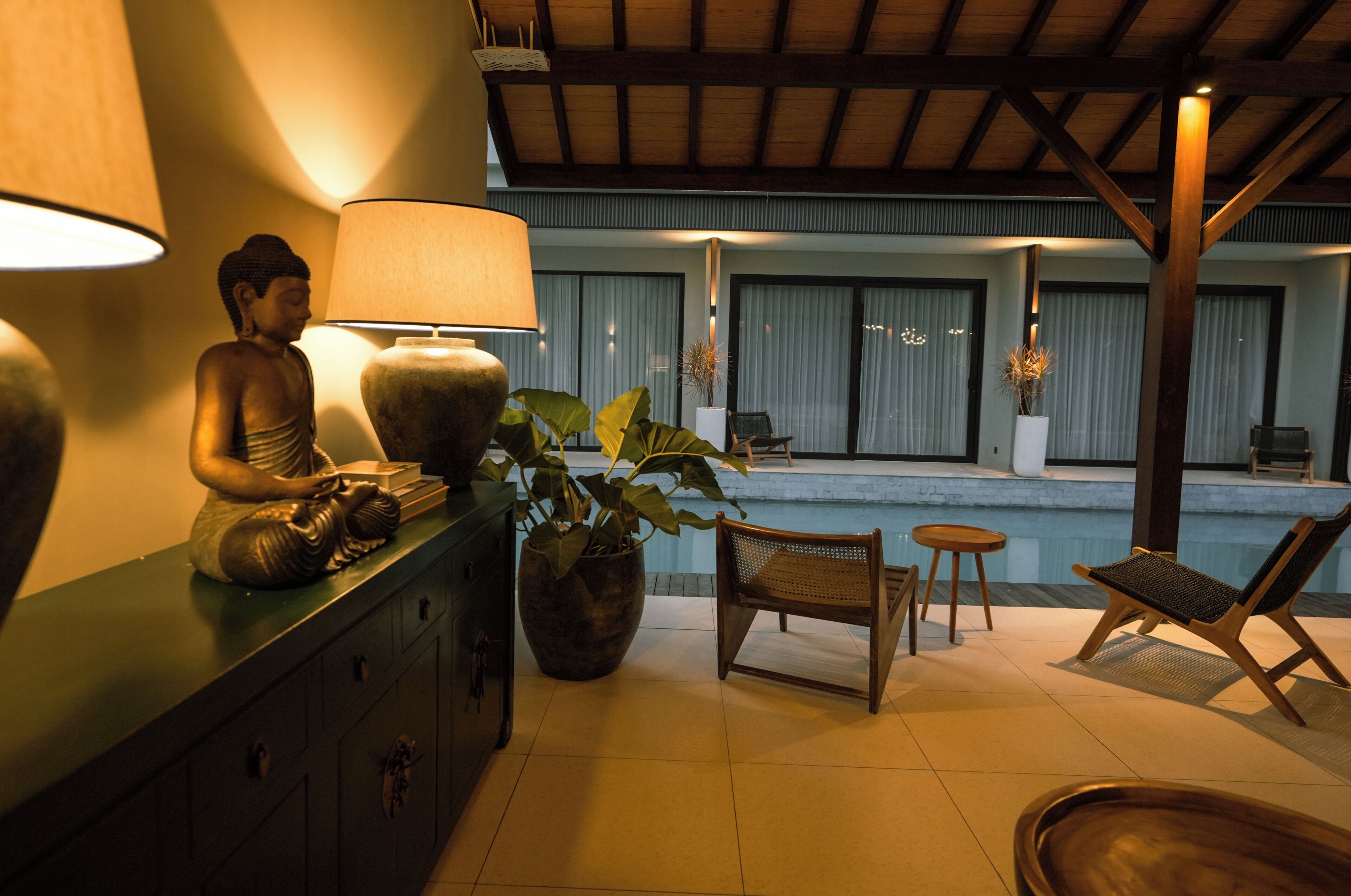 A serene indoor setting with a Buddha statue, a lamp, and a pool area.