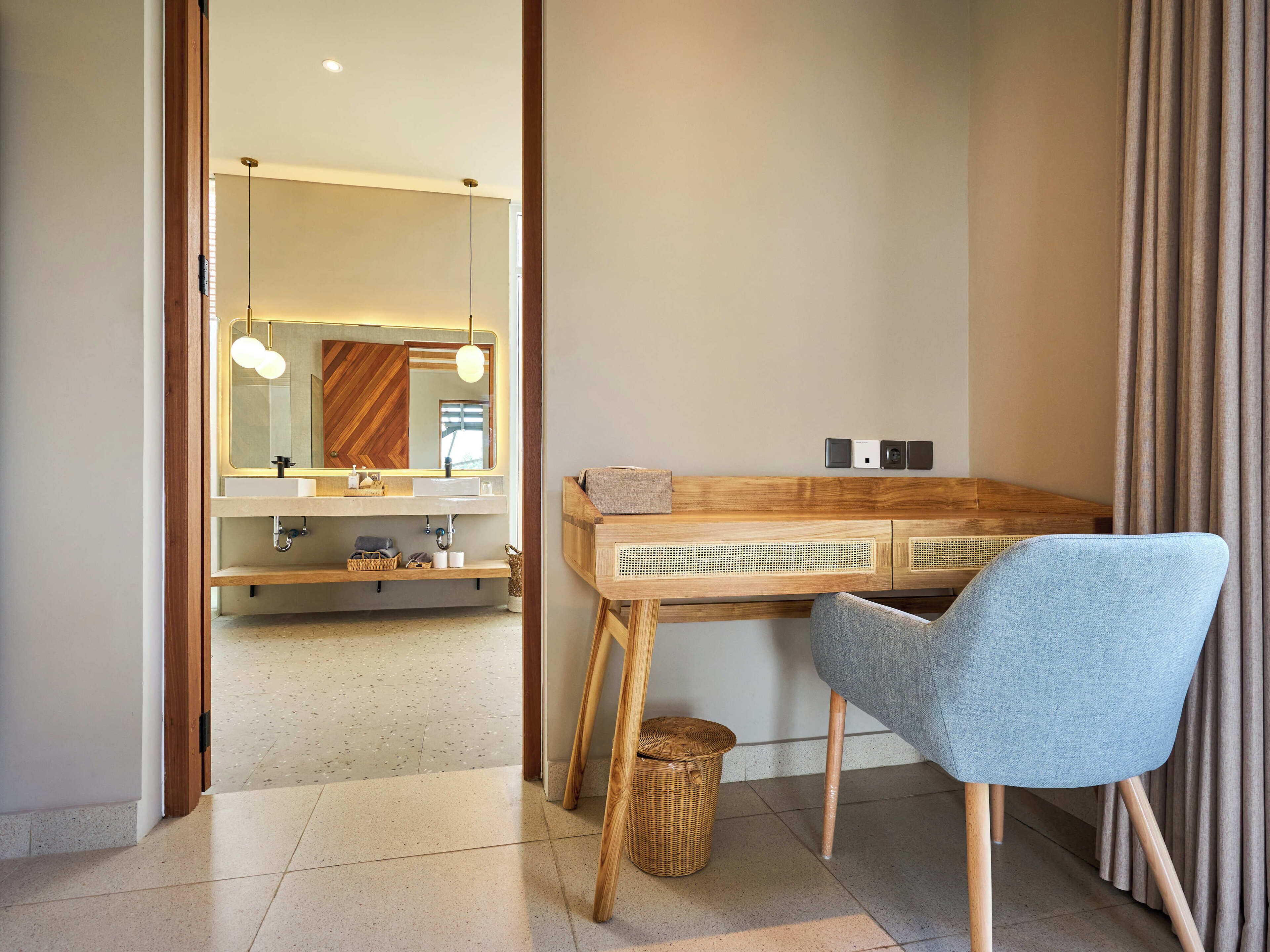 Un baño moderno con tocador de madera, un espejo con luces redondas y una silla azul.