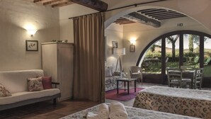 A cozy room with a sofa, two beds with floral bedding, a wooden cabinet, and a view of an outdoor patio with a table and chairs. - ONE-ROOM APARTMENTS 8 COLLE VAL D’ELSA  (Casole d'Elsa)
