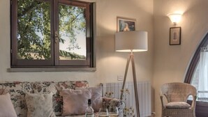 A cozy living room with a floral sofa, a standing lamp, and a wicker chair. - ONE-ROOM APARTMENTS 8 COLLE VAL D’ELSA  (Casole d'Elsa)