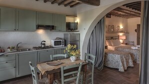 A compact kitchen with a dining area, a TV, and a bedroom with a bed and bedside table. - ONE-ROOM APARTMENTS 8 COLLE VAL D’ELSA  (Casole d'Elsa)