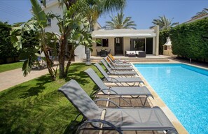 A poolside area with lounge chairs and a building in the background. - Soothing Sunset Villa, 200m to the Beach (Pervolia)