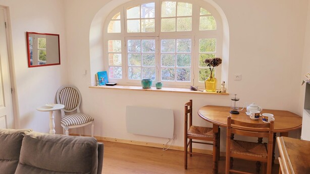 A cozy room with a large arched window, a small table with chairs, a radiator, and a mirror on the wall.
