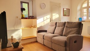 A living room with a beige sofa, a wooden coffee table, a laptop, and a vase with flowers.