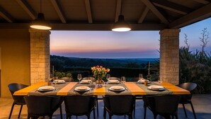 An outdoor dining area with a table set for six, surrounded by stone pillars, overlooking a scenic landscape.