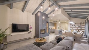 A modern living room with a large flat-screen TV, a fireplace, and a dining area with a long table and chairs.