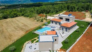 A modern two-story house with a swimming pool, surrounded by a well-maintained garden and fields.