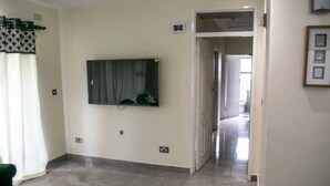A room with a flat-screen TV mounted on the wall, a door leading to another room, and a tiled floor.