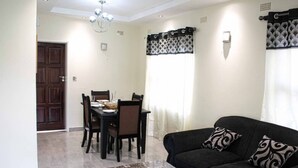 A living room with a dark sofa, a coffee table, and a dining area with a table and chairs.