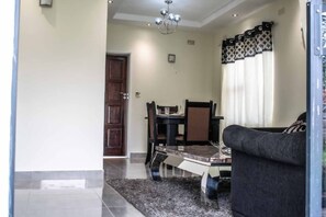 A living room with a sofa, a dining table with chairs, a chandelier, and a door.