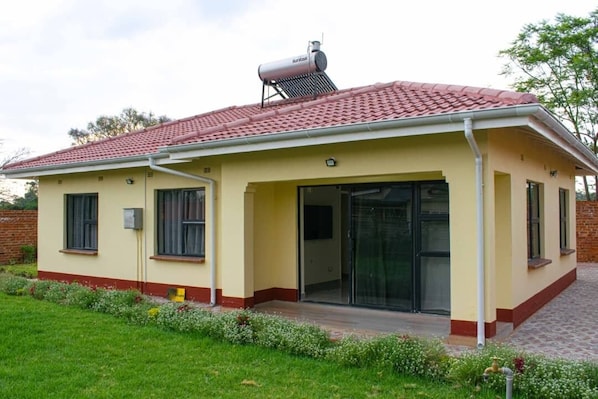 A single-story building with a red-tiled roof, a covered patio area, and a small garden with flowers.