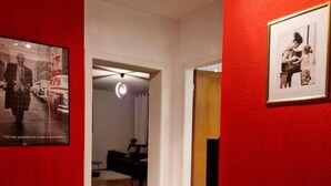 Un couloir aux murs rouges, doté d’un plancher en bois et orné de tableaux encadrés.