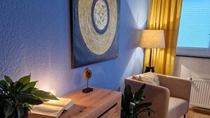 Une pièce avec un mur bleu, un bureau en bois doté de tiroirs, un canapé beige, un rideau jaune et une fenêtre avec des stores.