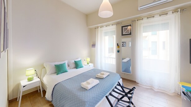 A bedroom with a bed, nightstands, a lamp, a mirror, and a window with curtains. - Guest House Sonnino 37 Cagliari (Cagliari)