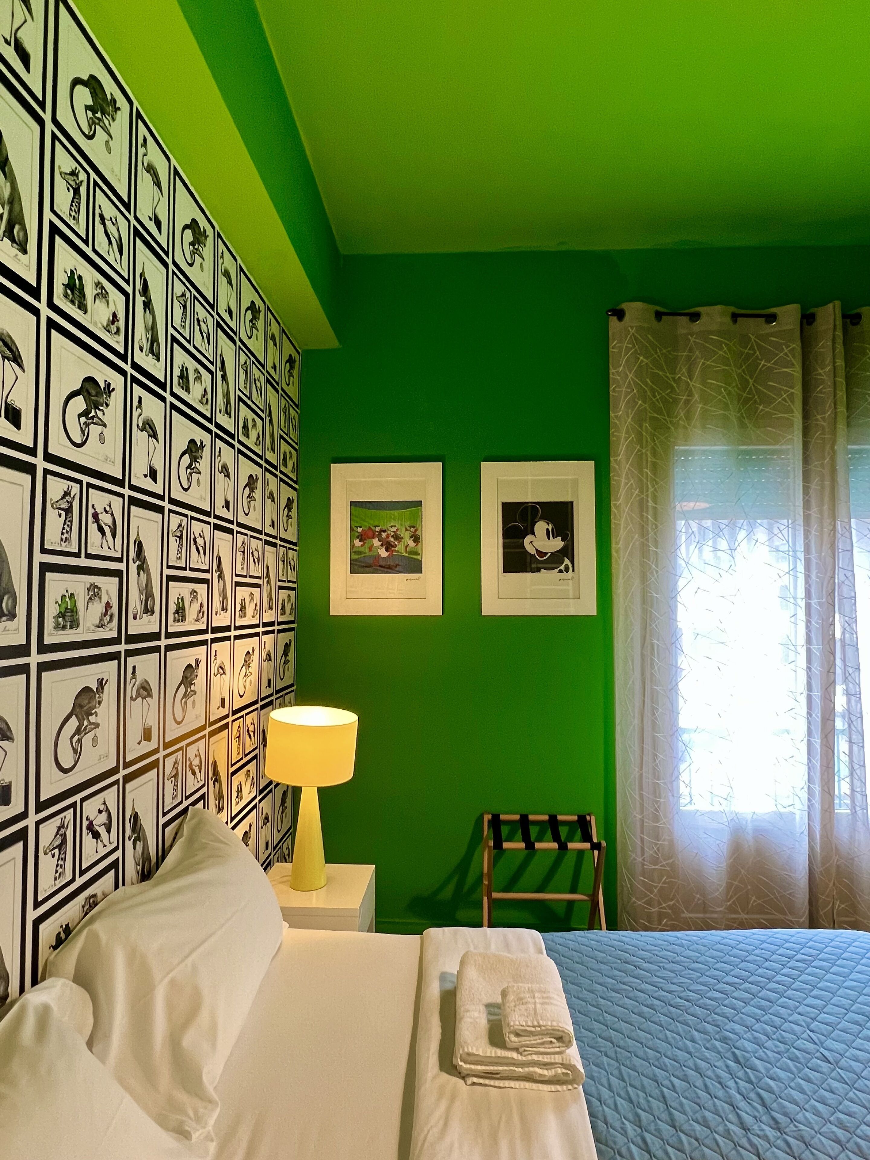 A room with a green wall, a bed with white bedding, a lamp, and framed pictures on the wall.