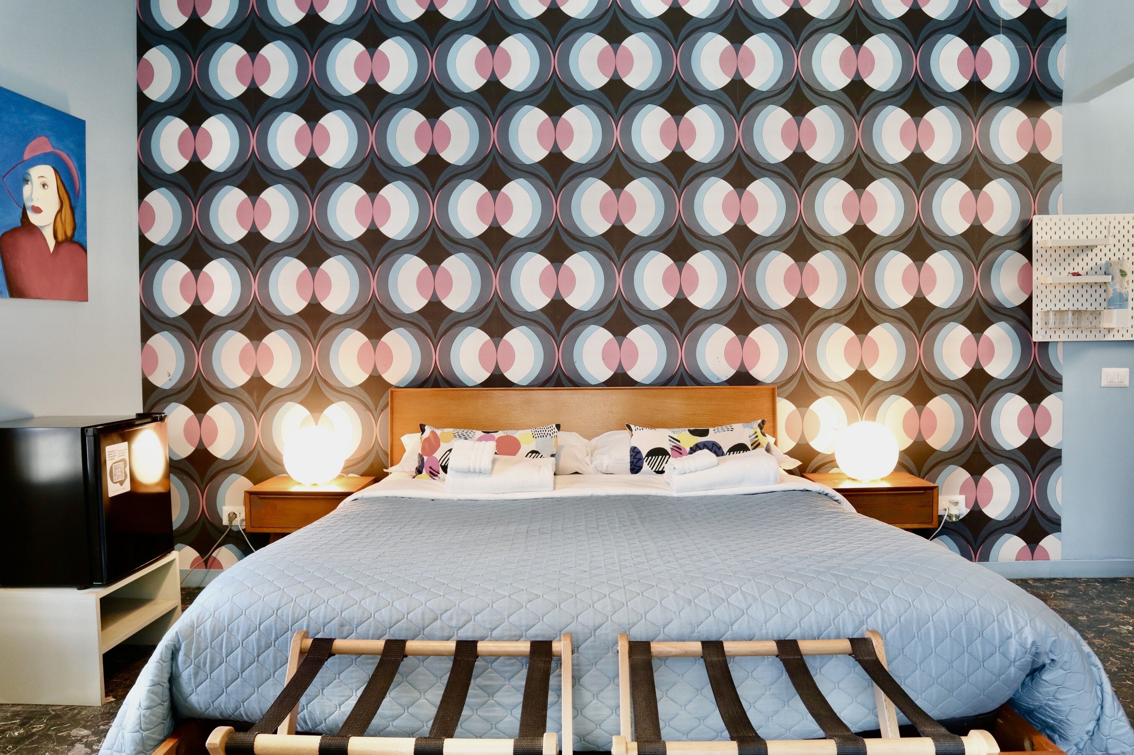 A hotel room with a bed, bedside tables, a TV, and a patterned wall.