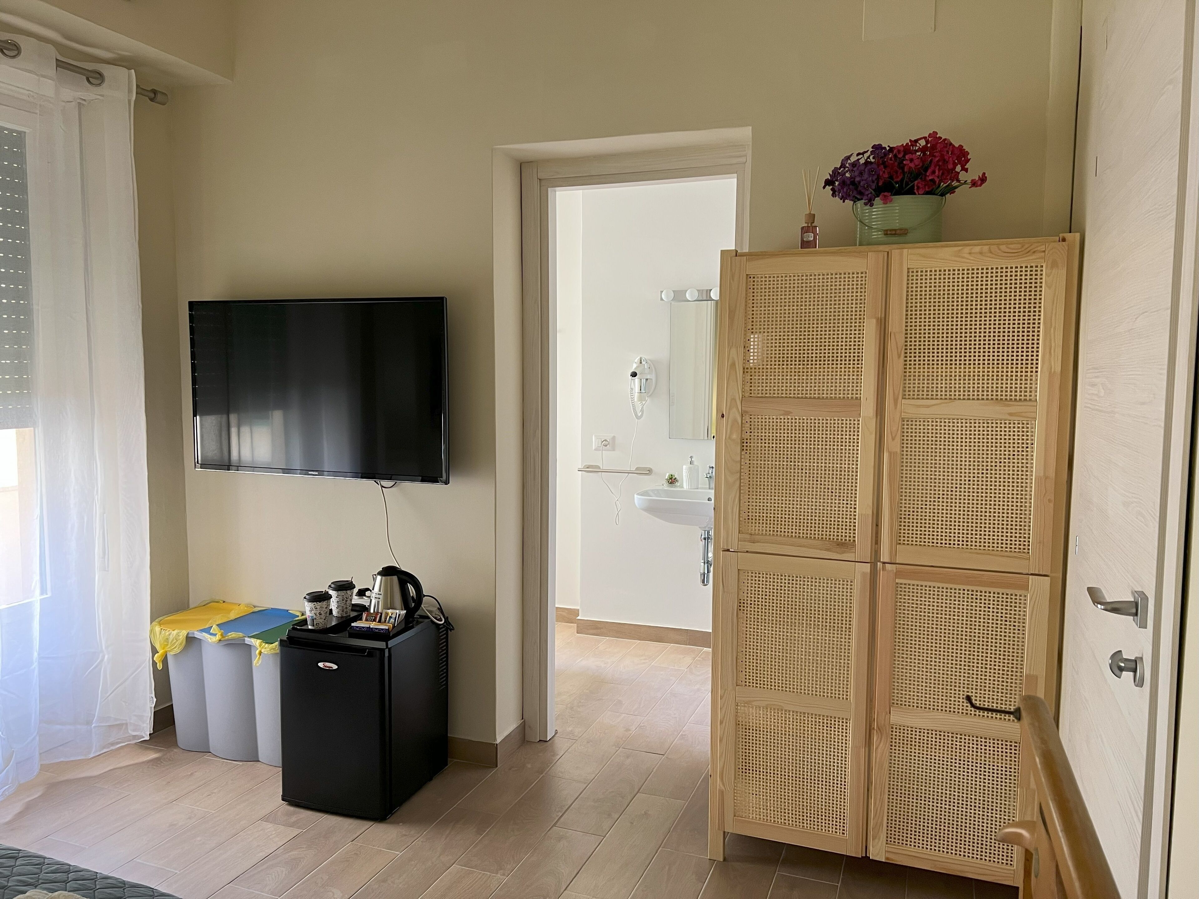A room with a television, a small black refrigerator, a wooden cabinet, and a door leading to a bathroom.