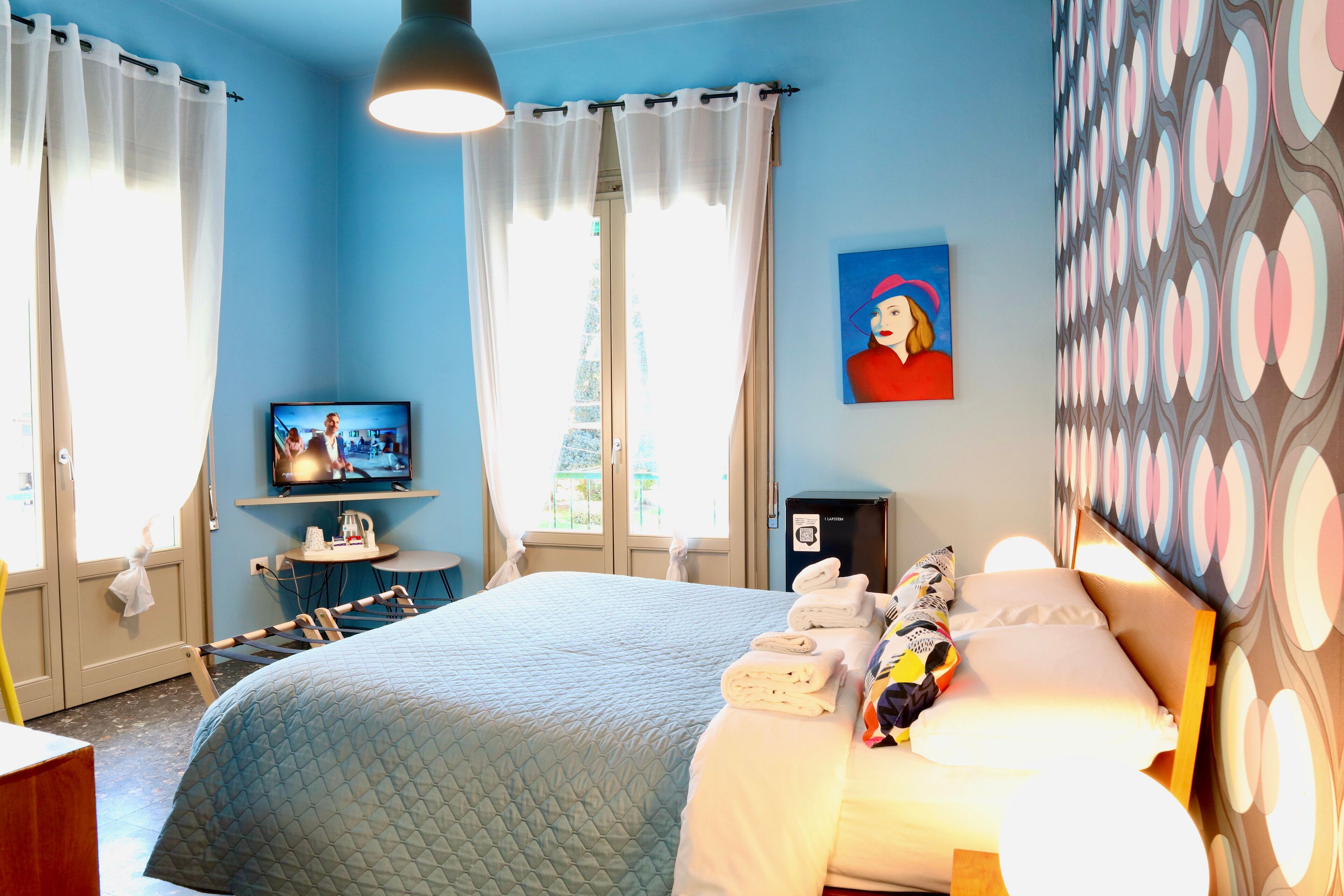 A hotel room with a large bed, a television, a desk with a chair, and a painting on the wall.