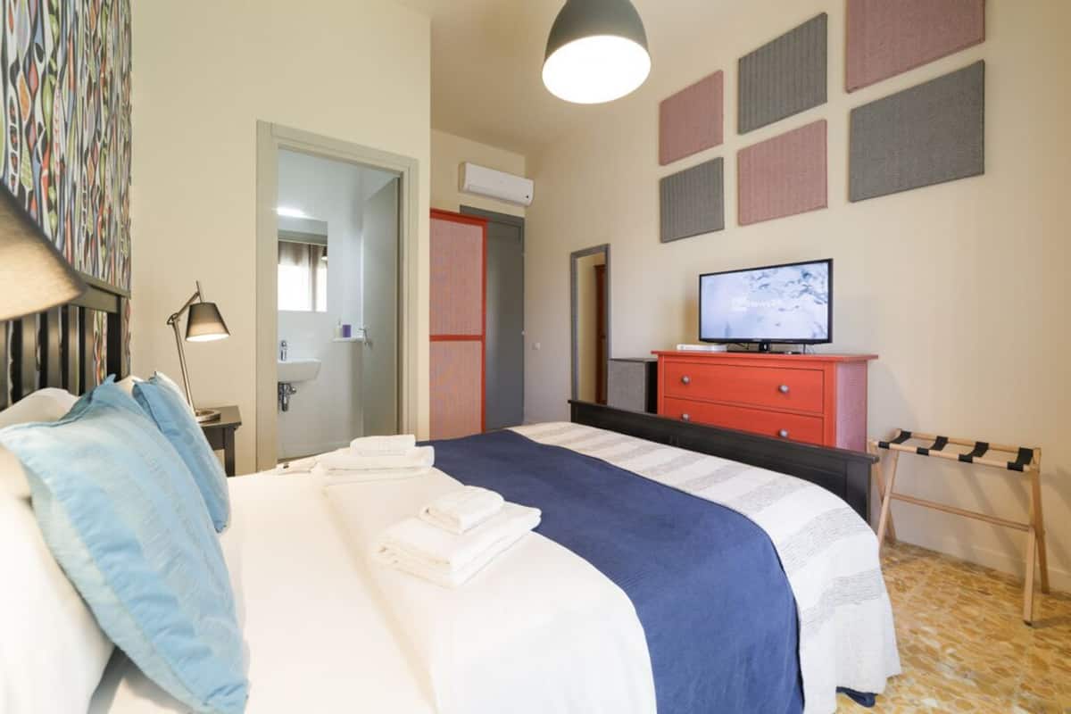 Una habitación de hotel con una cama, televisor, cómoda roja y sistema de sonido integrado en la pared.